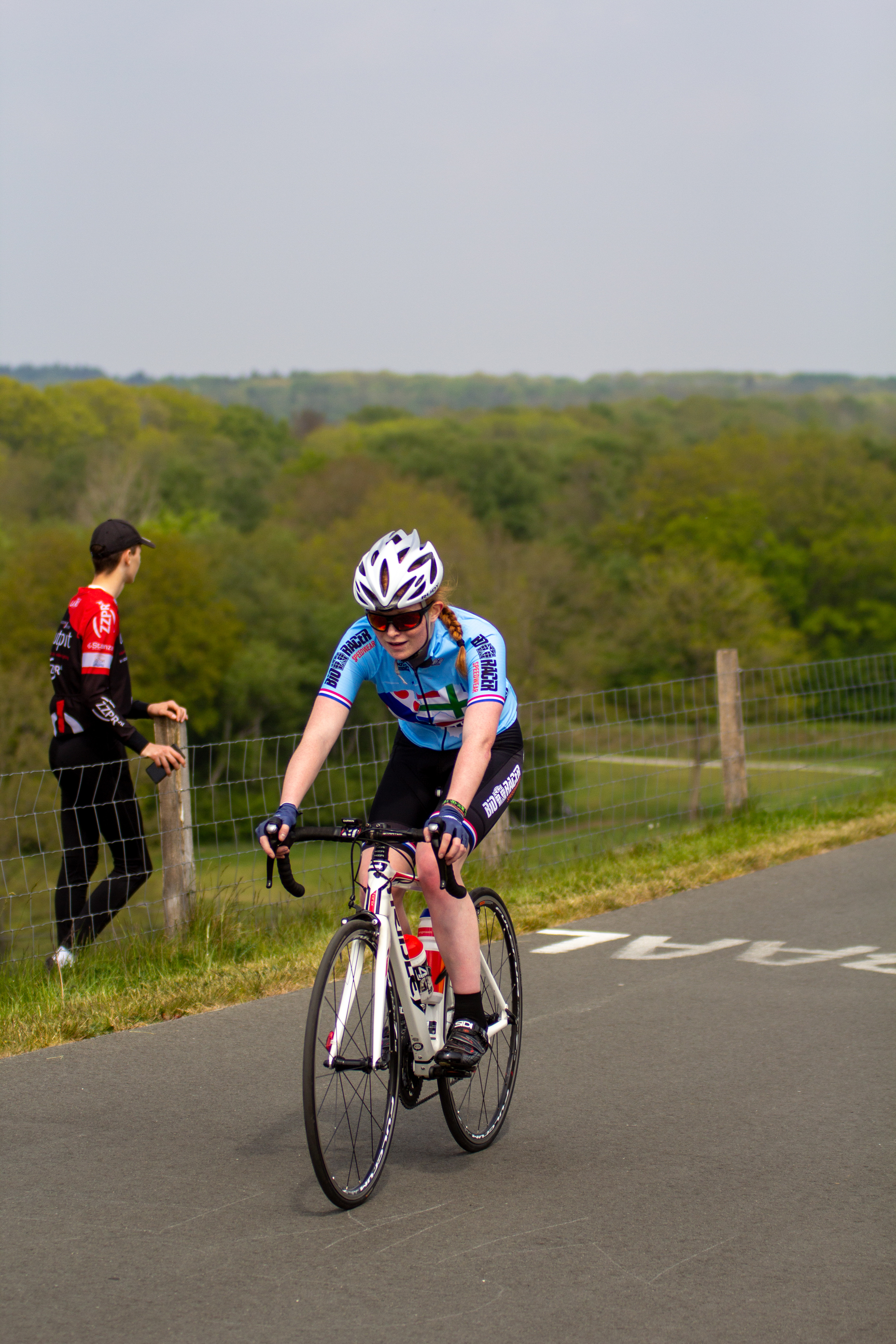 A woman wearing a blue bike jersey is riding a bicycle on a road.