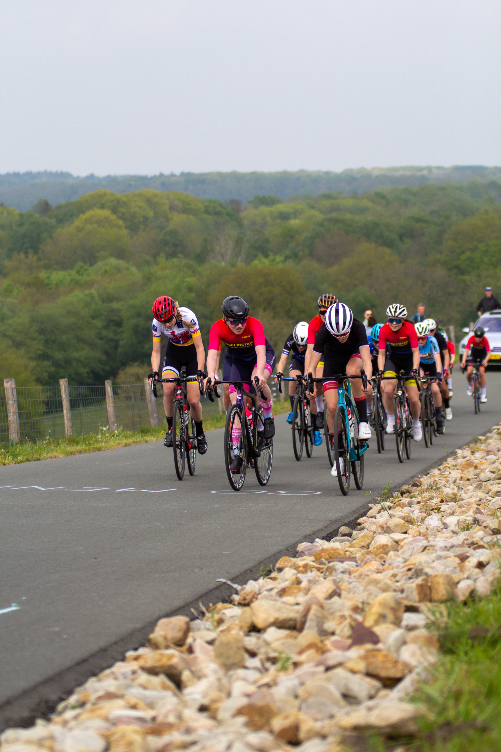 A group of cyclists wearing helmets and riding bikes on a road during the Dames Criterium.