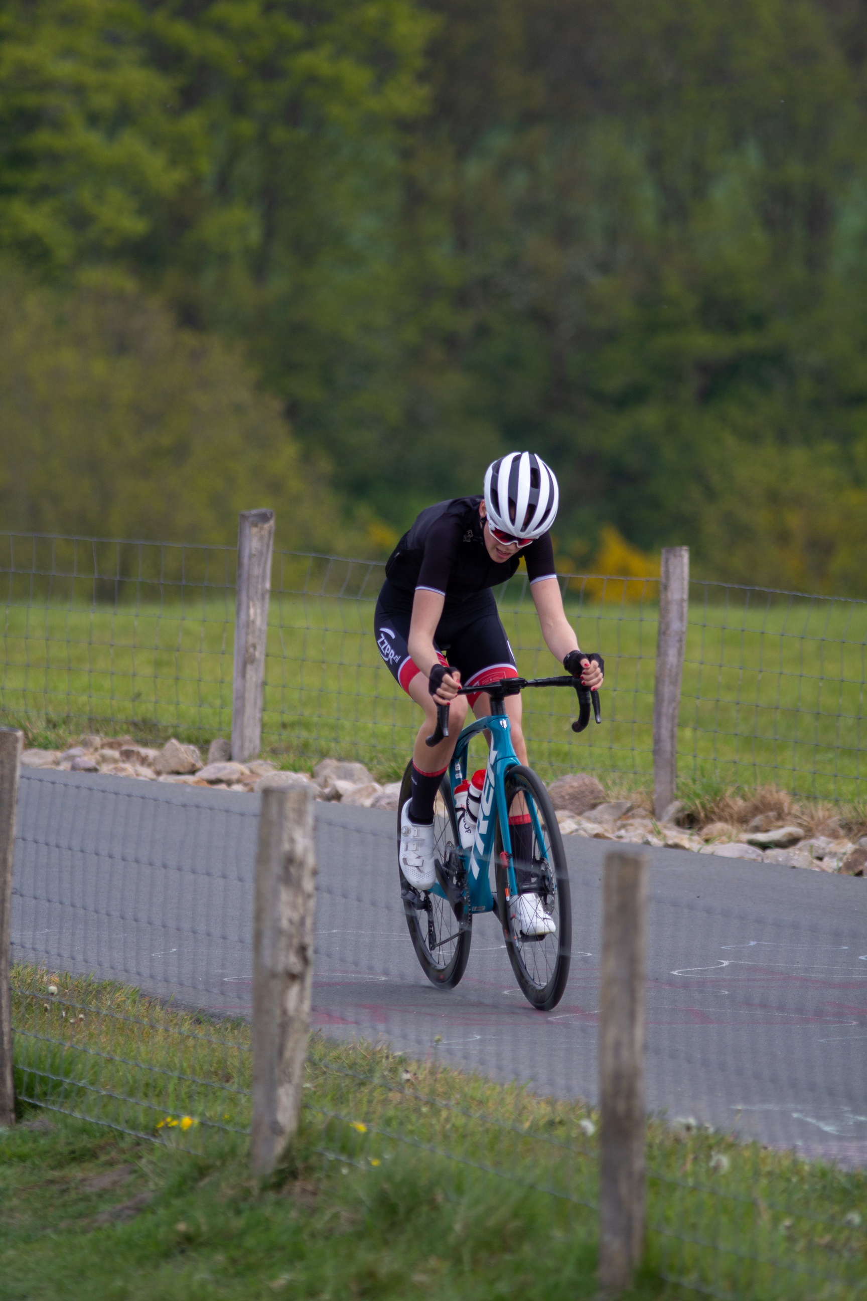 A young man wearing a black and white outfit rides his blue bicycle on the road.