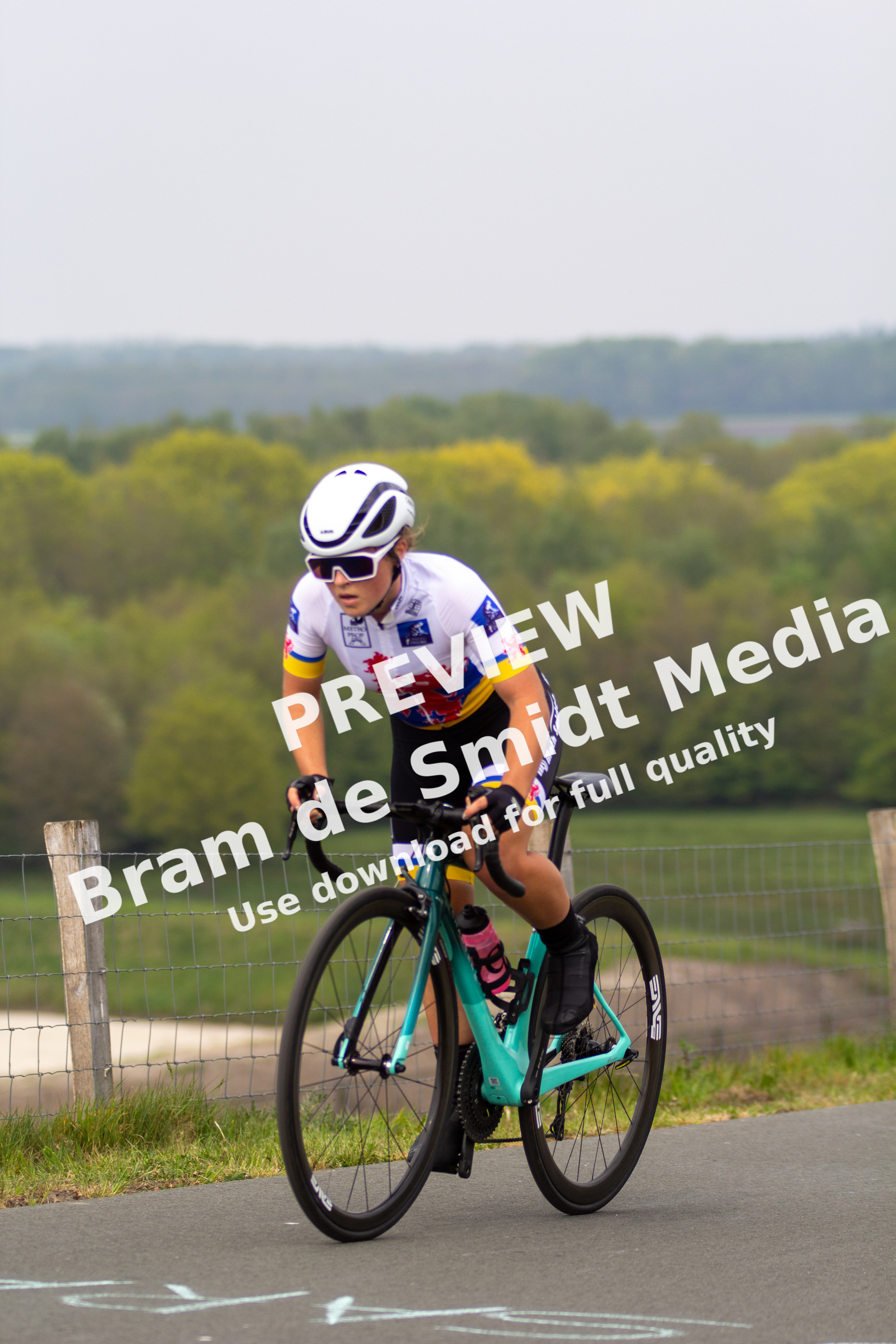 A female cyclist is wearing a white helmet and riding on the road.
