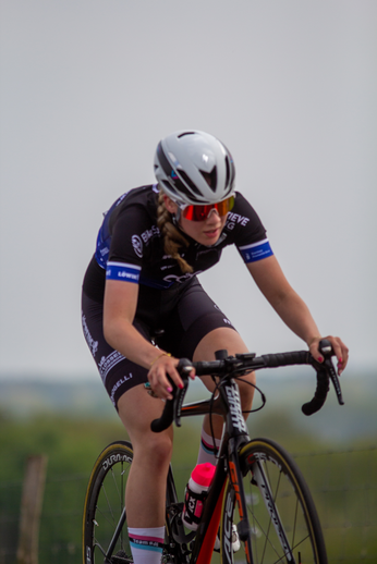 A cyclist wearing a black racing suit and helmet is riding a red and white bike.