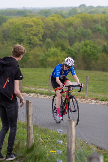 A woman riding a bike with the number 3 on her back. She has a helmet and is dressed in black, red, and blue.