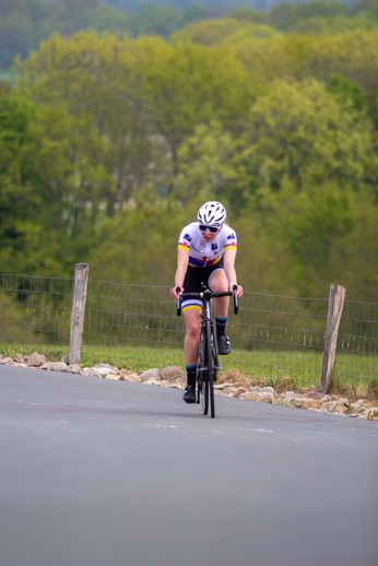 A woman wearing a purple, black and white jersey is riding her bike on a road.