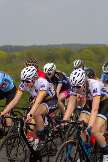 A group of cyclists wearing white and black jerseys with logos for the Dames Criterium race.