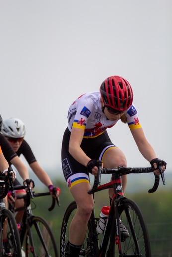 A female cyclist in red and white racing gear, sponsored by Bollinger.