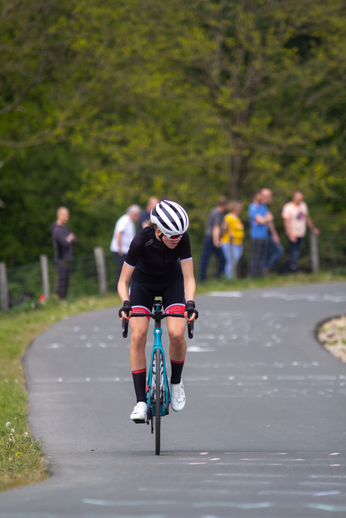 A woman in a black jersey with red stripes on her knees rides a bicycle down the street.