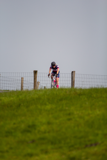 A woman in a purple and white uniform rides her bike in the Dames Criterium.