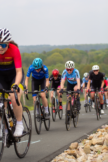 A group of cyclists race through a grassy field during the Tweedaagse Wielrennen Dames.