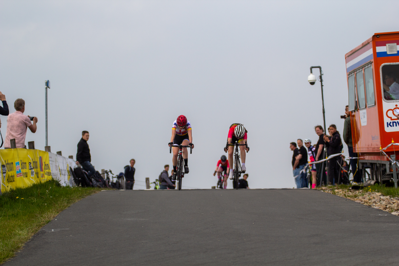 Three bicyclists are racing each other in a race sponsored by the company Coll du Vam.