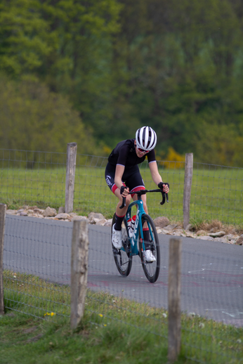 A young man wearing a black and white outfit rides his blue bicycle on the road.