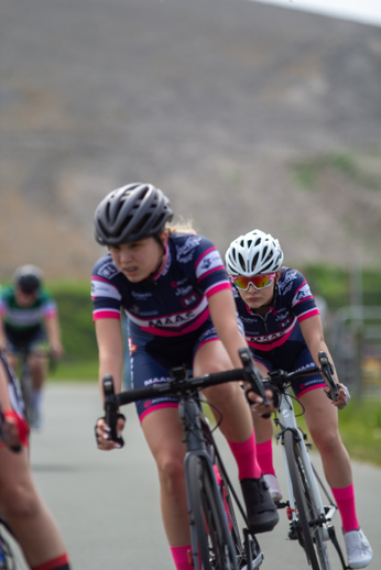 Two women wearing helmets are riding bikes in a race.