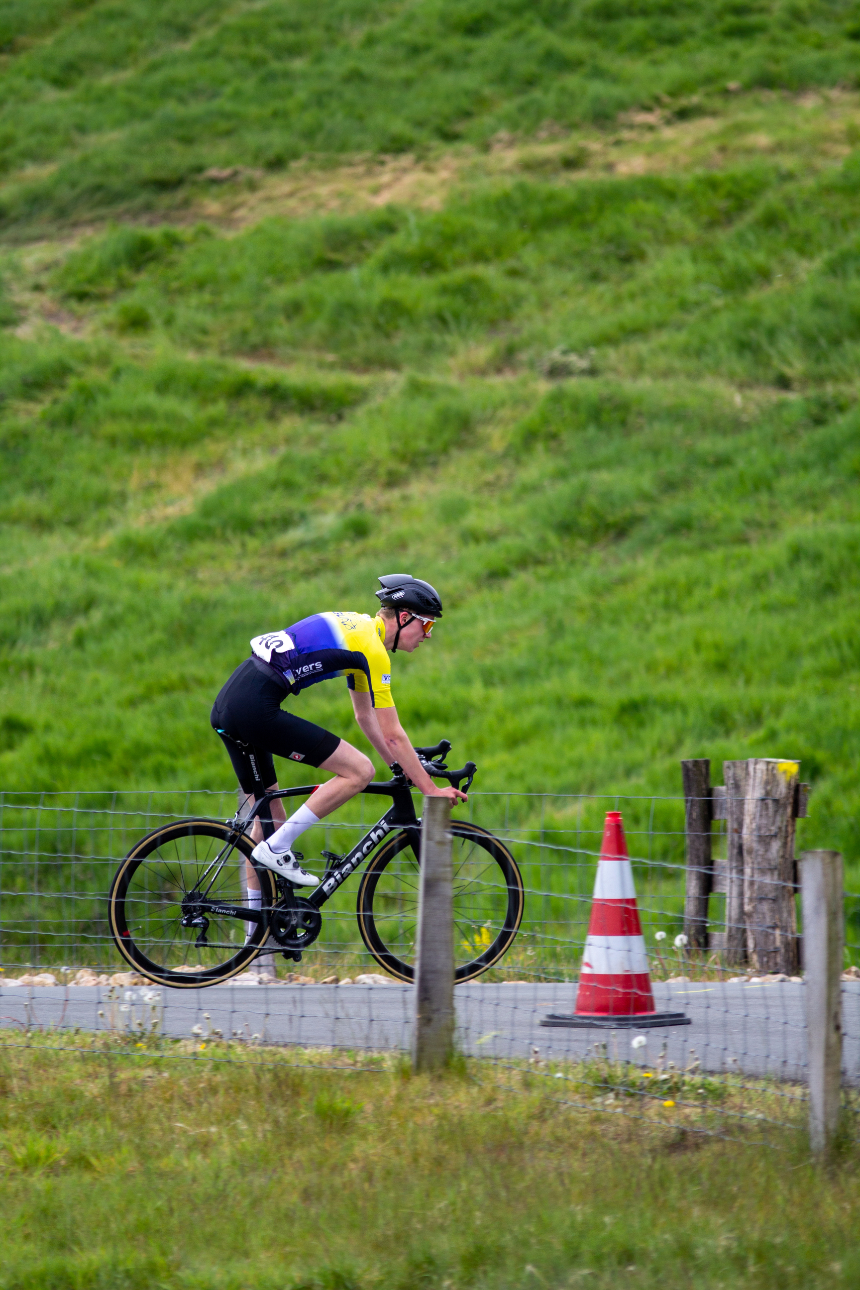 A cyclist racing through a course of cones and barriers, in a field with a hill in the background.