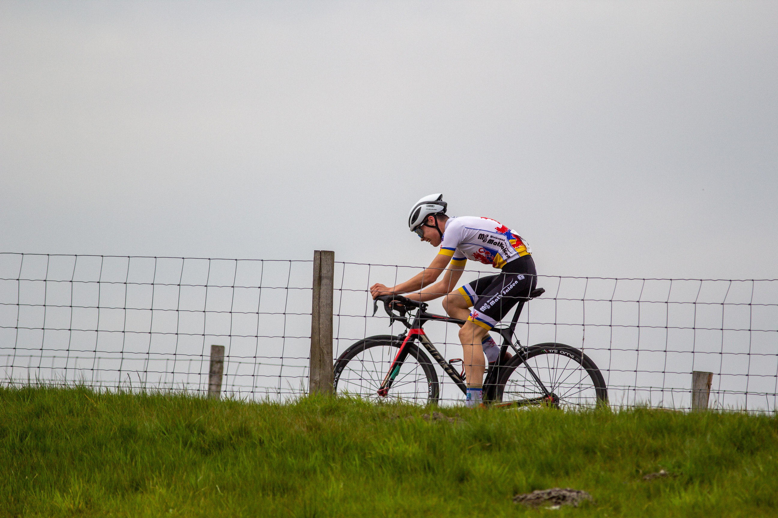 A man rides a bicycle along the top of a grassy hill.