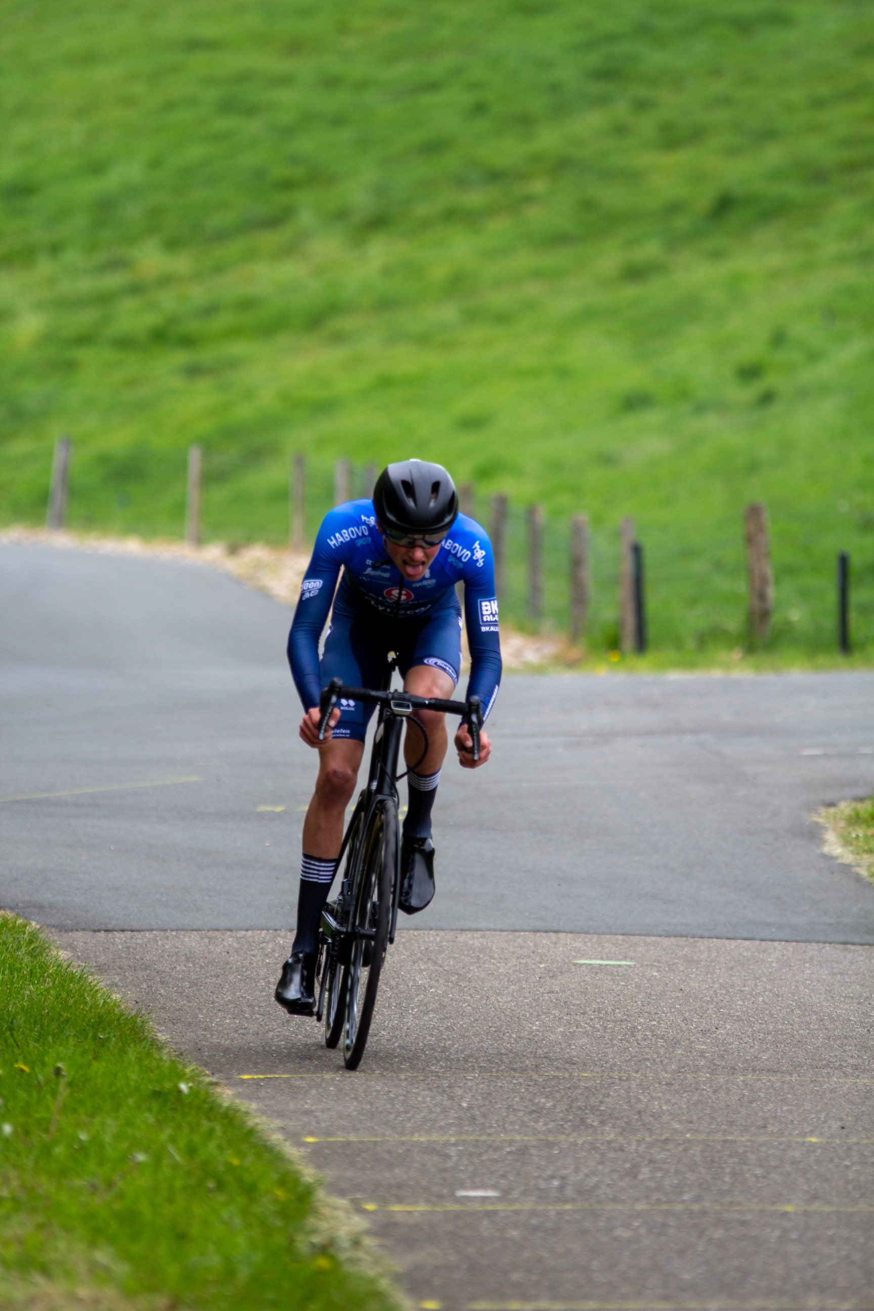 A man wearing a blue and white cycling uniform is riding his bike down a road.