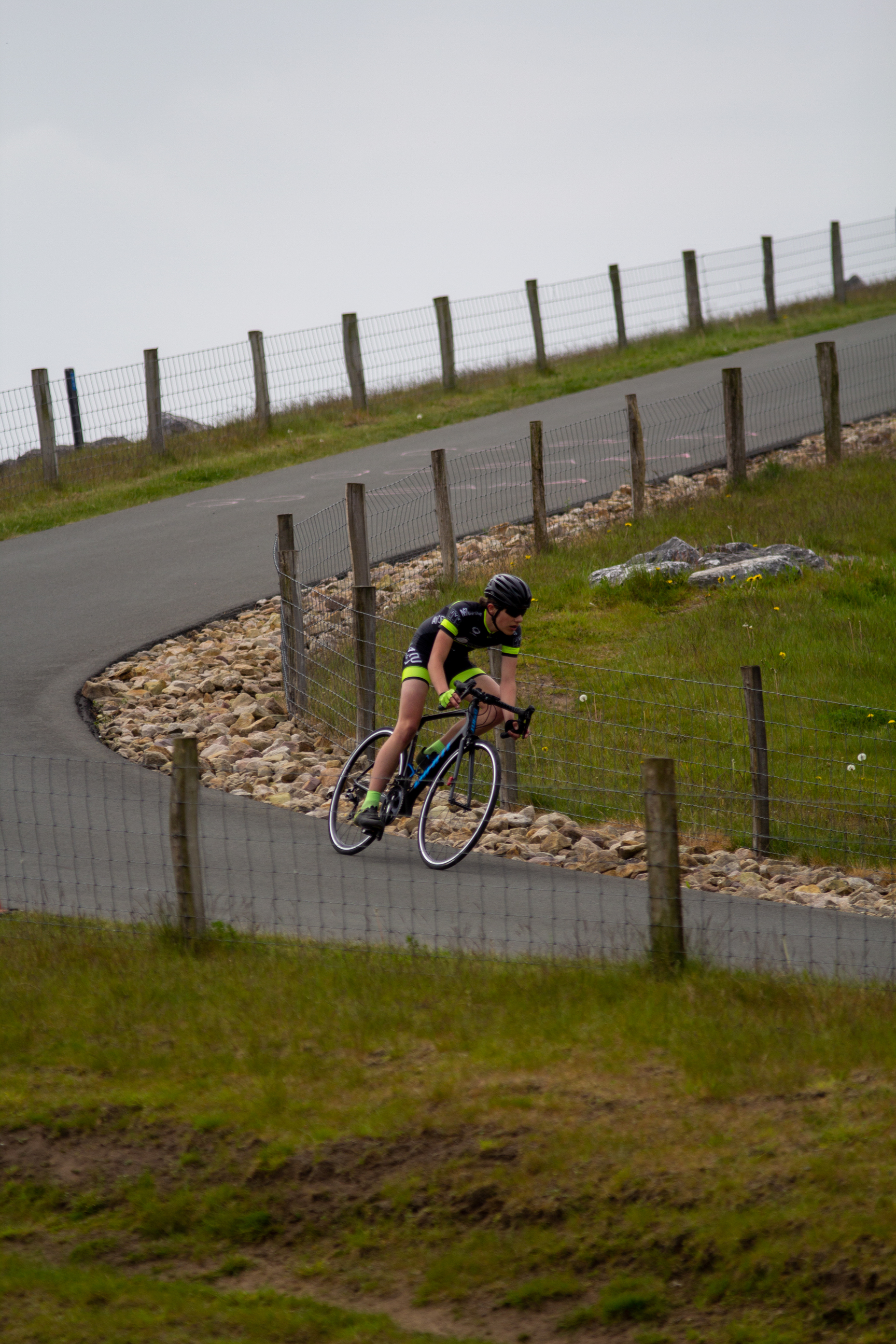 A female cyclist wearing a black jersey and helmet riding her bicycle down a steep hill.