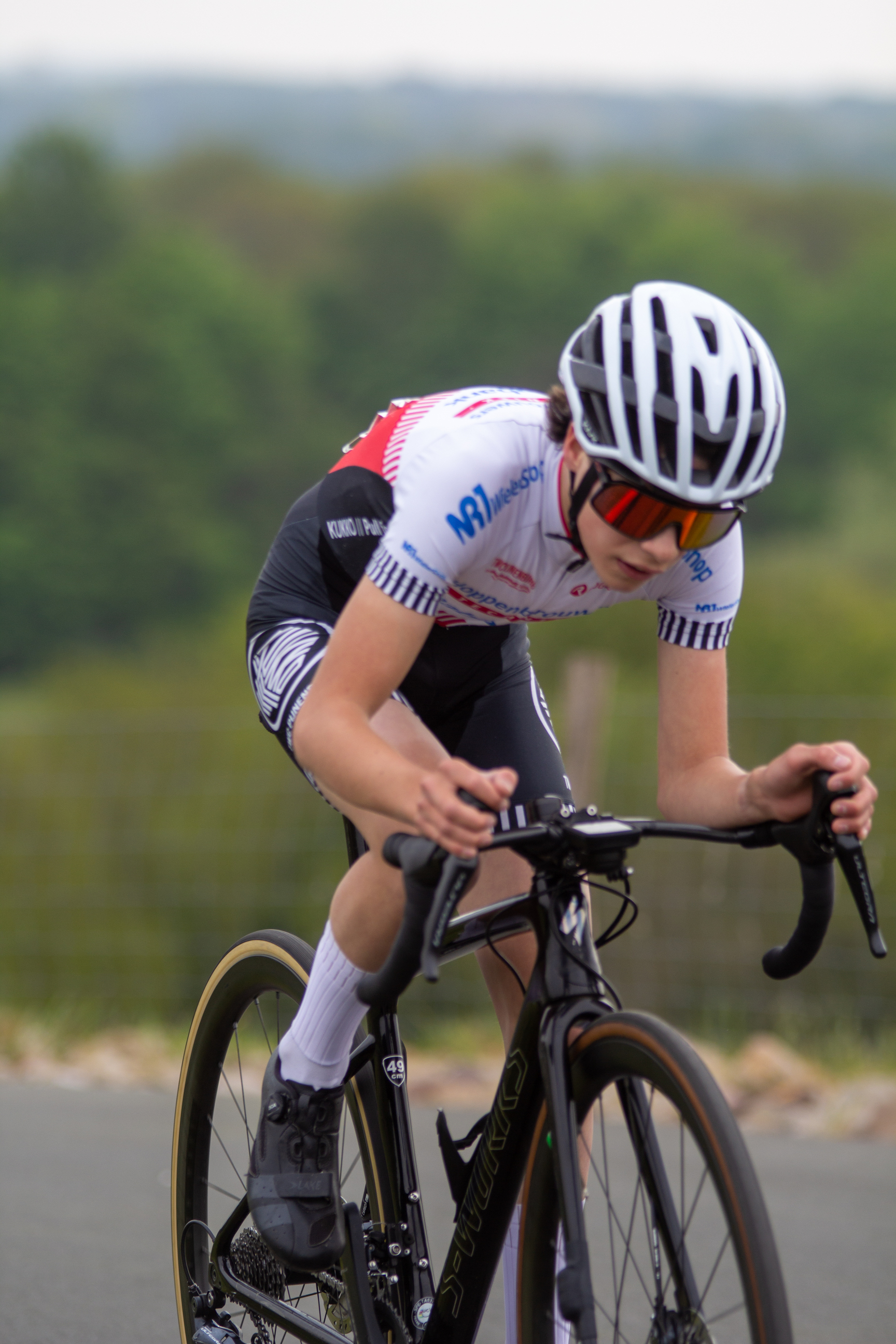 A young cyclist wears a white and red jersey as he navigates the roads with his hands on the handlebars.