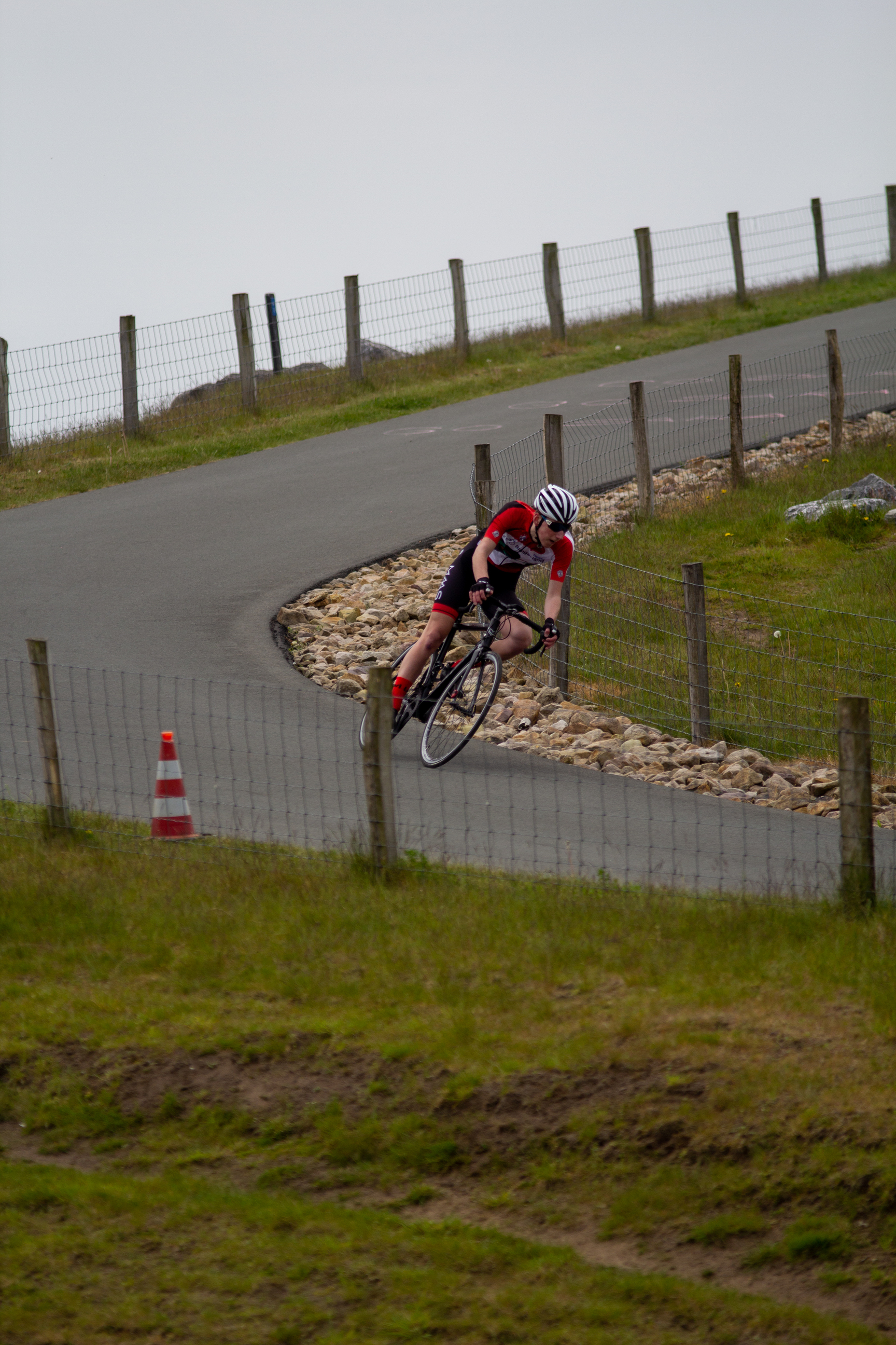 A cyclist rides down a winding road on a cloudy day.