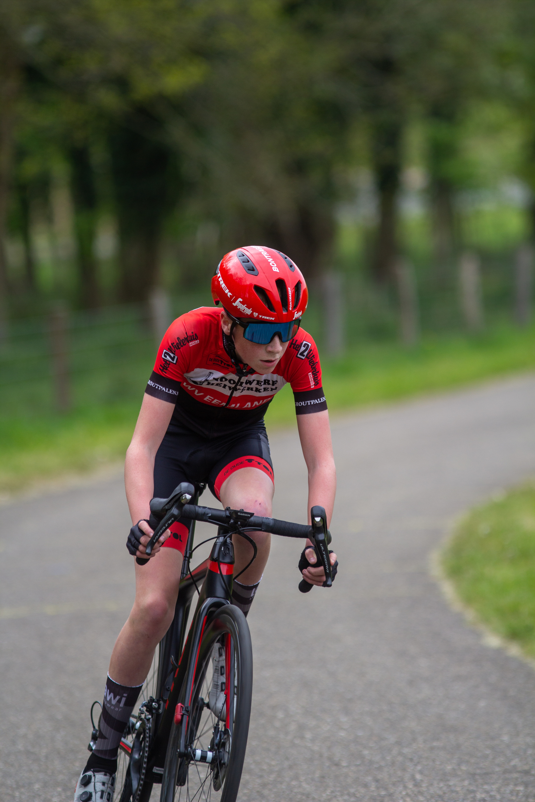 A young man is racing on a bicycle wearing red and black clothing.