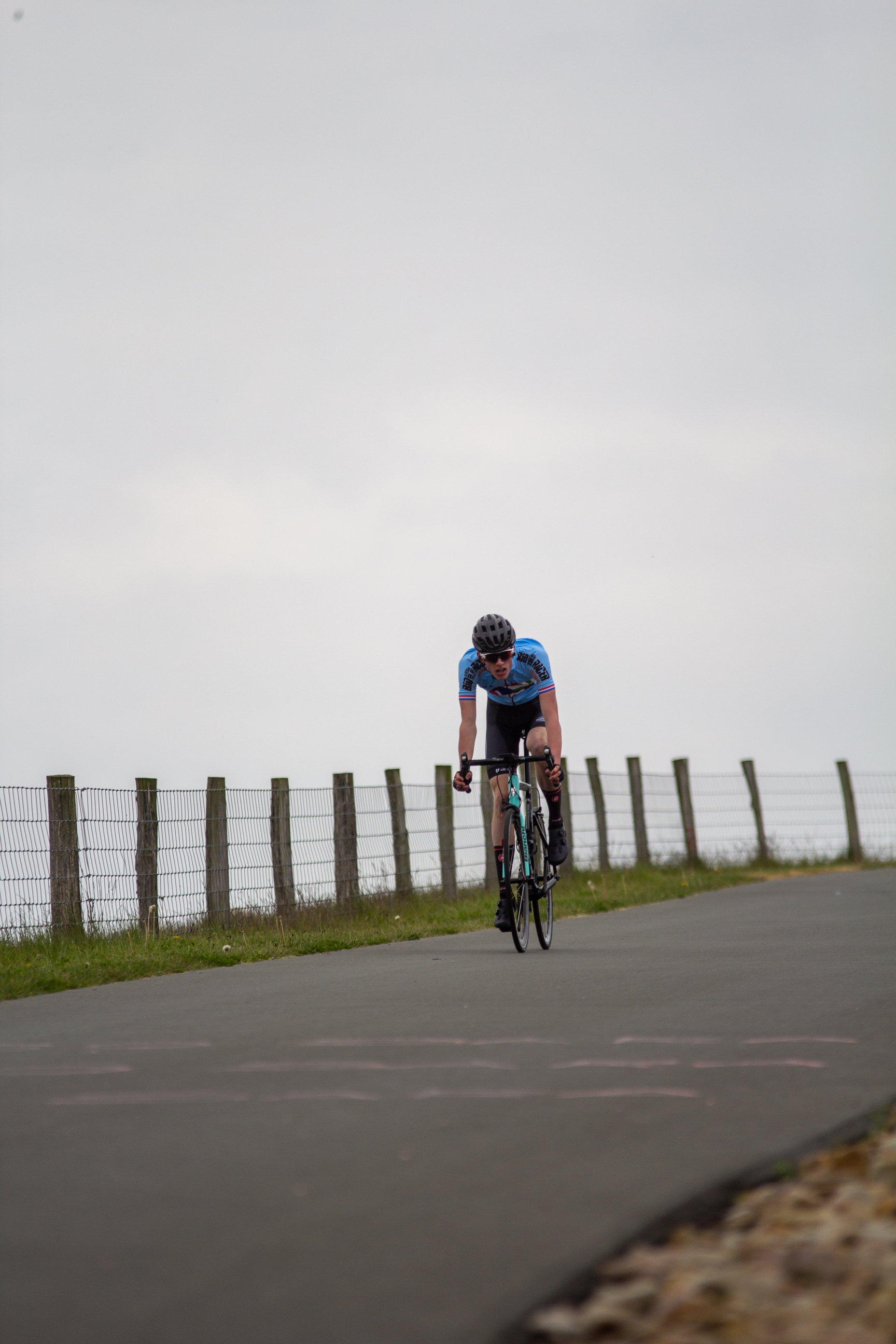 A man wearing a blue shirt and black helmet riding his bicycle down the road.