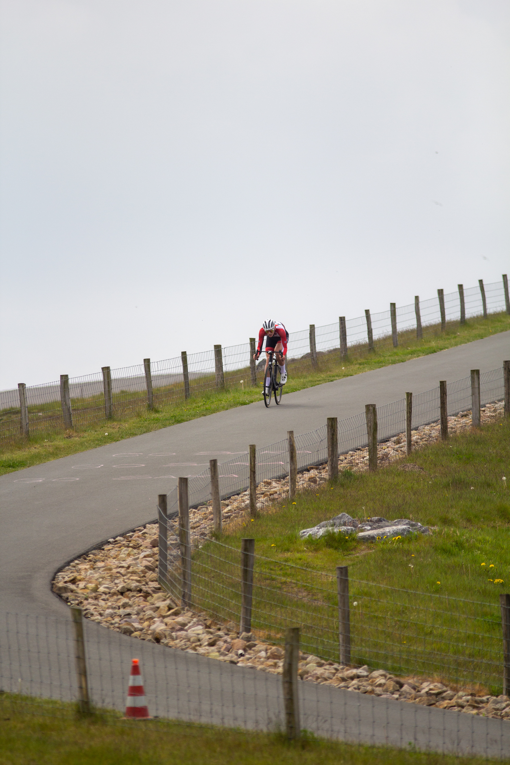 A cyclist in a red jersey races down a hill with grass on the sides.