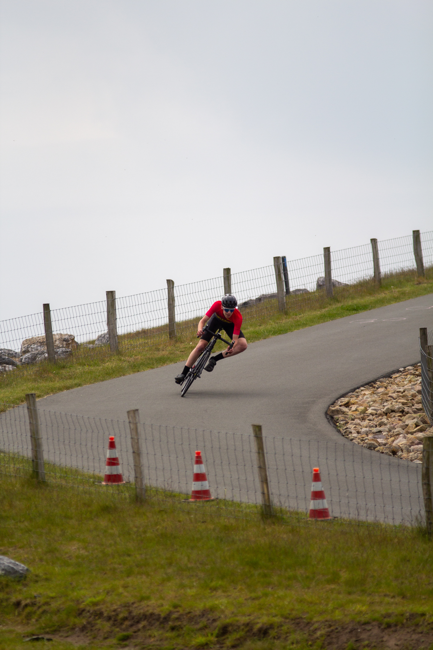 A cyclist racing down a hill with orange traffic cones lining the side of the road.