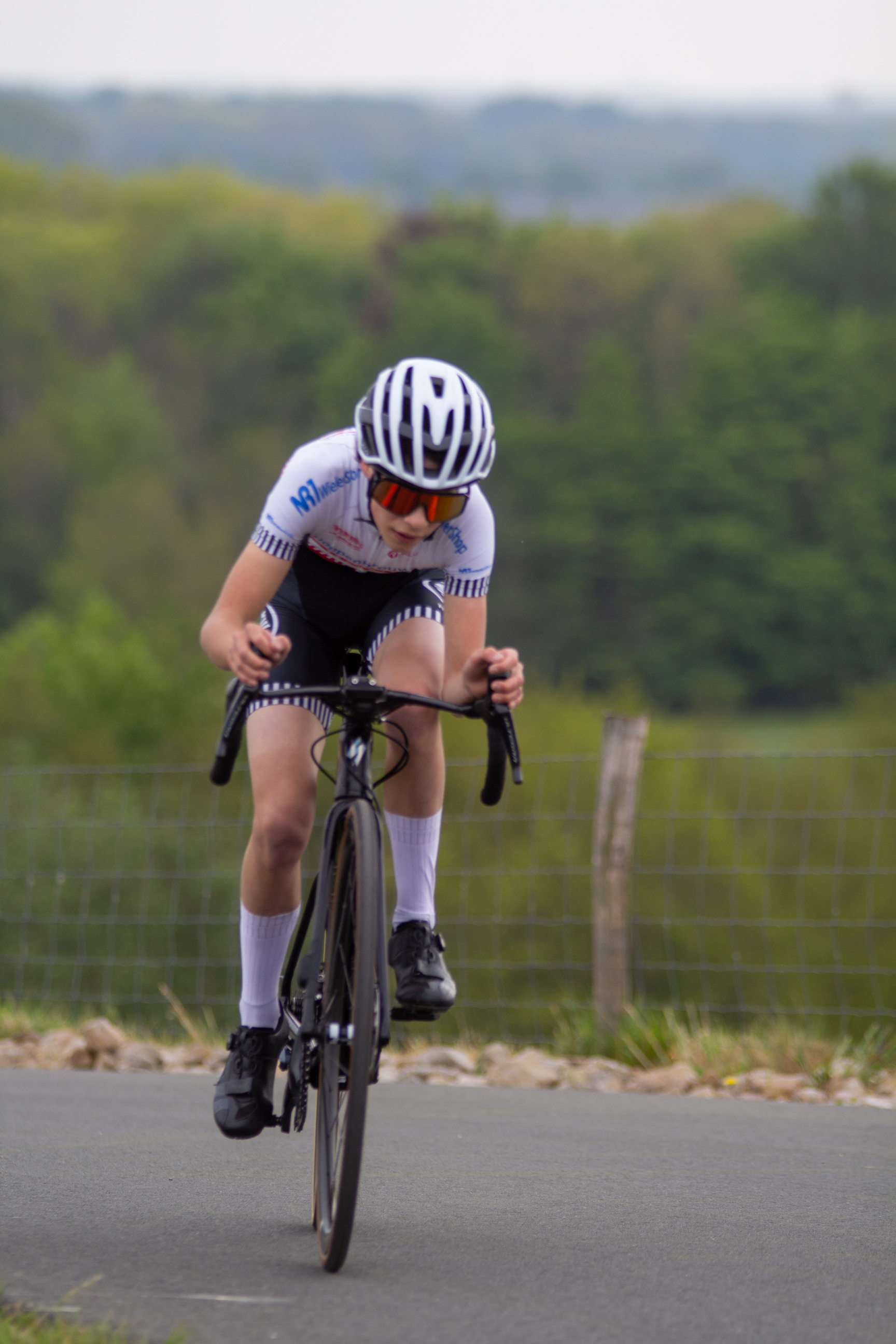 A man wearing a white shirt and helmet riding his bike down the road.