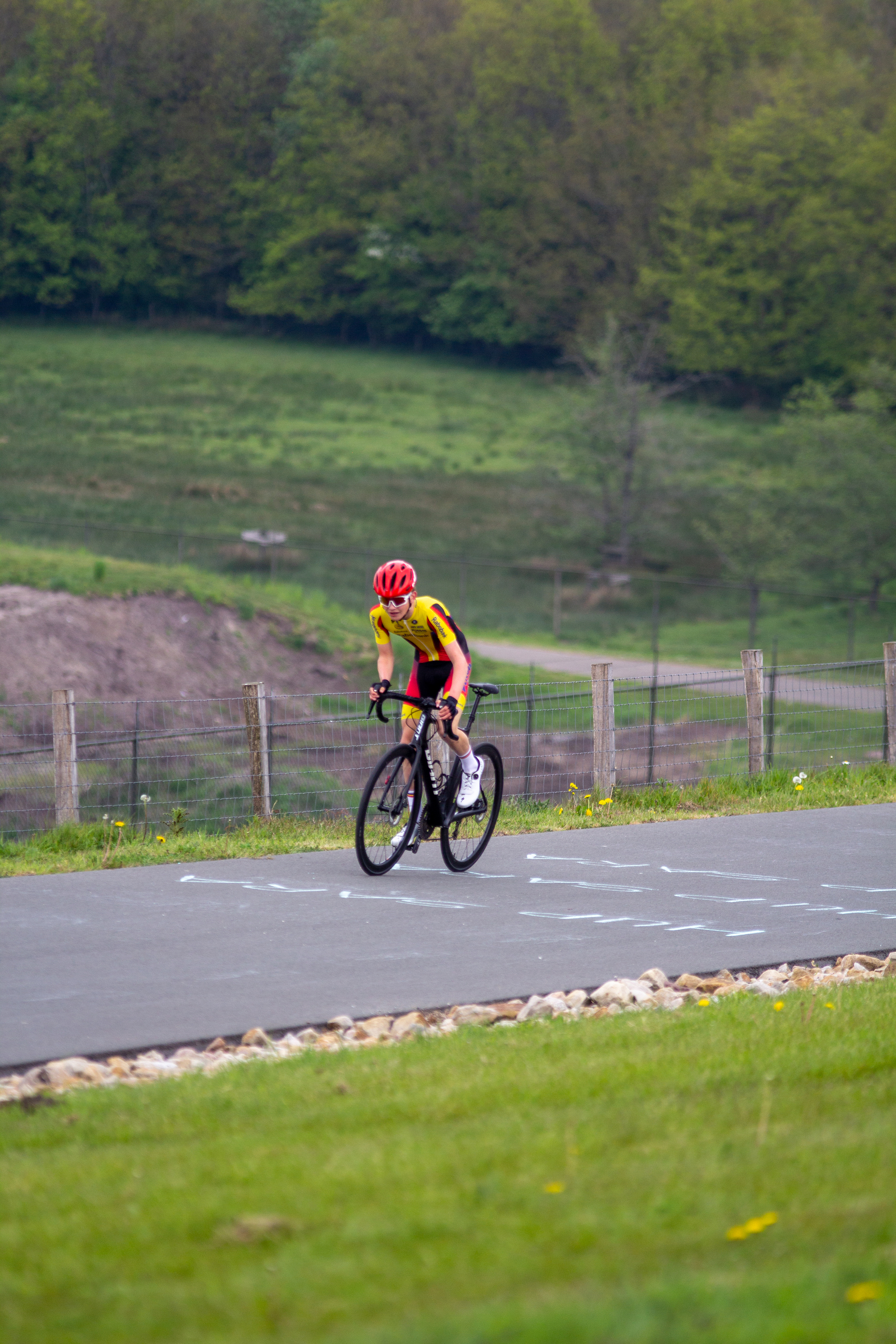 A cyclist in red and yellow wearing a helmet is riding his bike down the road.