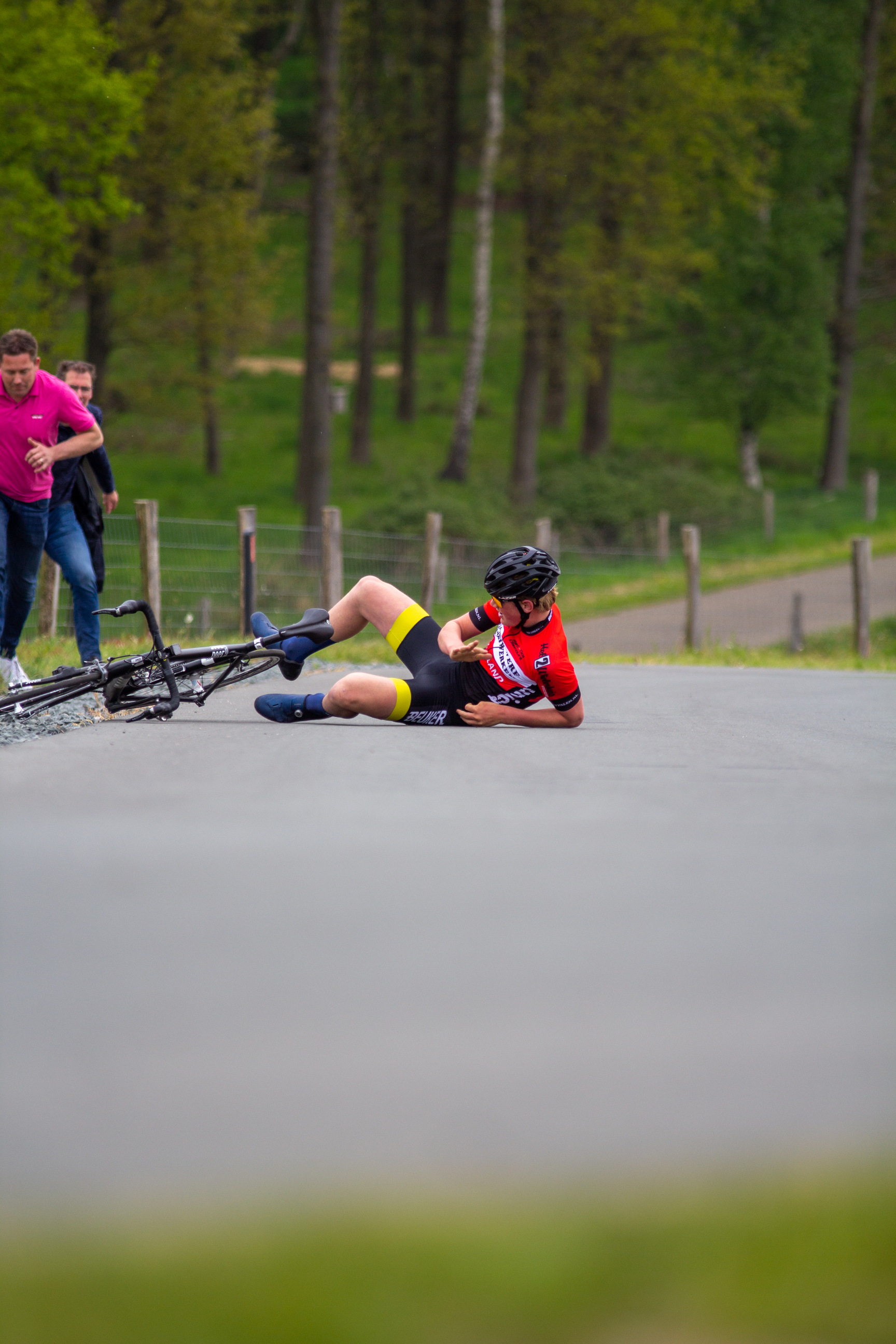 A woman wearing a red shirt and black shorts lies on the ground next to a bicycle.