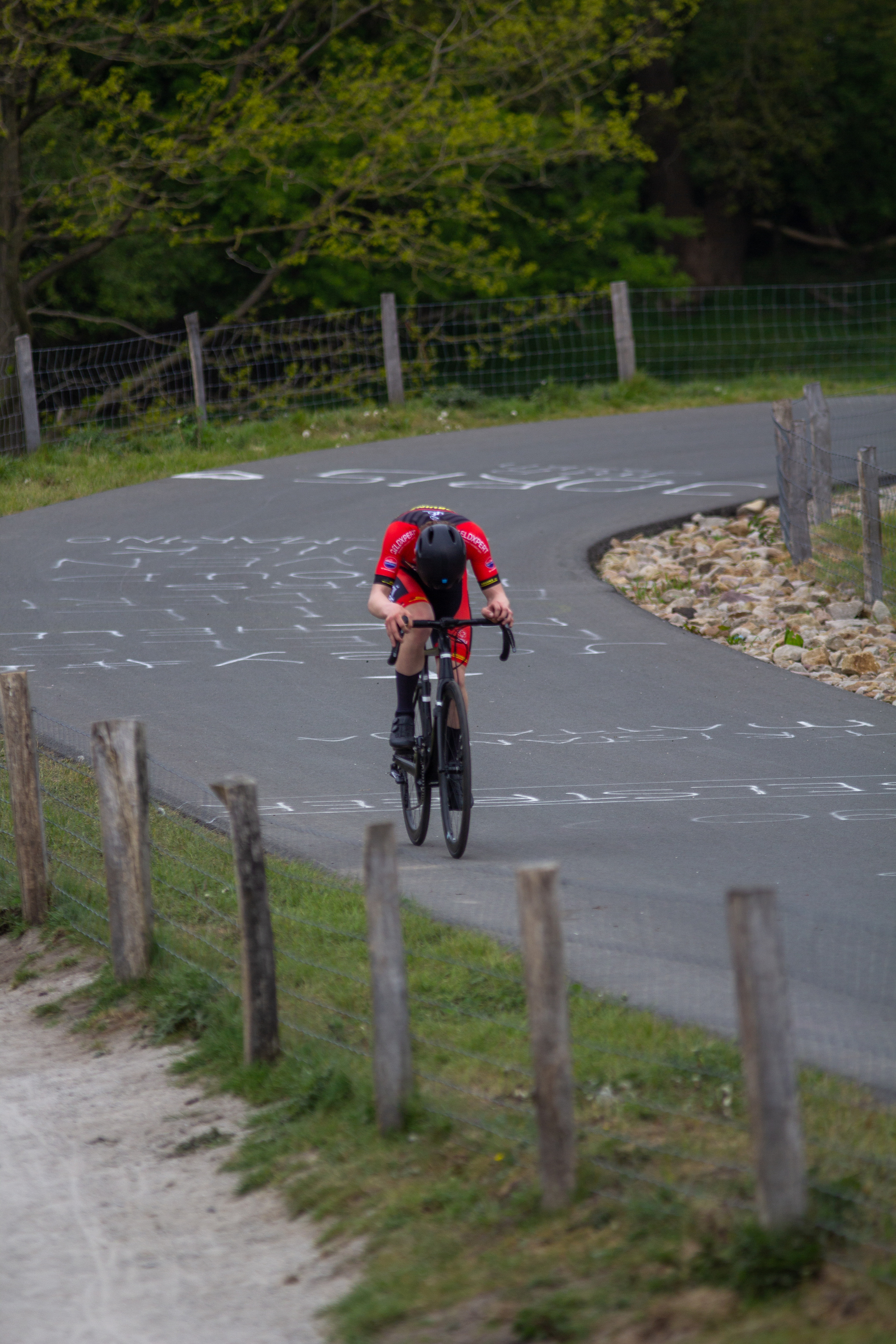 A man in a red shirt is on a bicycle next to some fences.