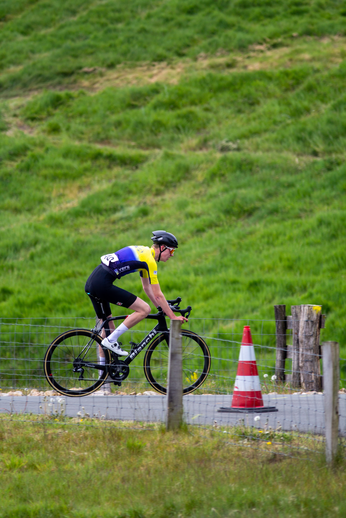 A cyclist racing through a course of cones and barriers, in a field with a hill in the background.