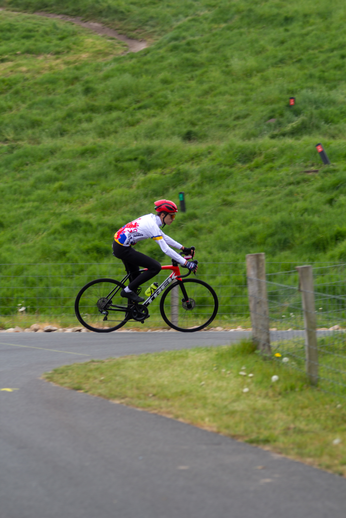 A cyclist in a white and red shirt is riding his bike down a hill.