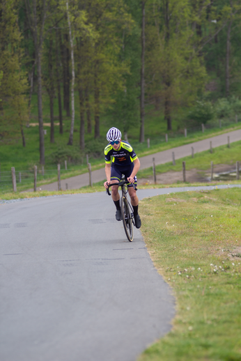 A man in a cycling race wears a black helmet with a logo.