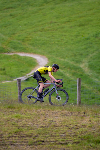 A cyclist wearing a yellow shirt and black helmet is riding his bicycle up a hill.