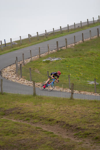 A cyclist in a black and red jersey rides down a hill.