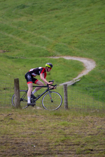 A man in a black and red shirt is riding a bike on grass. He has a yellow helmet on his head.