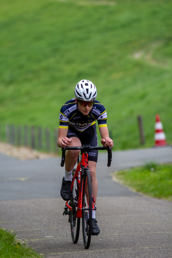 A cyclist in a yellow and blue jersey is riding a red and black bike on the road.