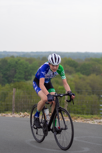 A man is riding a bicycle on a road, dressed in blue and green.