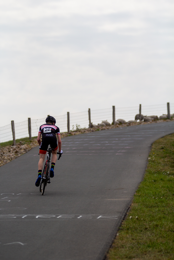 A man in a black and pink cycling outfit riding a bike on a road.