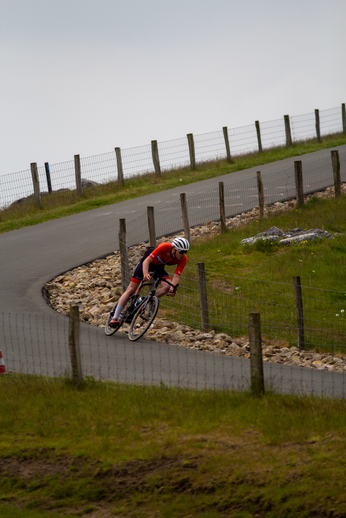 The cyclist in the red and black jersey is competing in a race on a windy day.