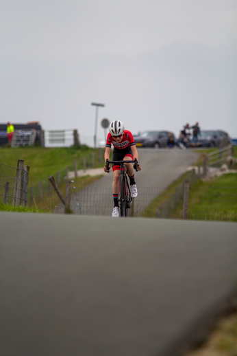 A cyclist wearing a white helmet with the number 12 on it races down a road past cars.