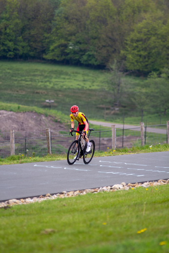 A cyclist in red and yellow wearing a helmet is riding his bike down the road.