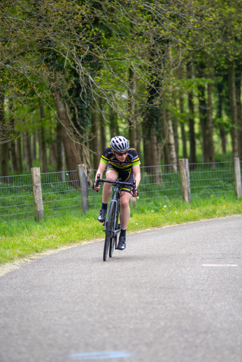 A female cyclist wearing a yellow jersey riding her bicycle down a tree-lined road.