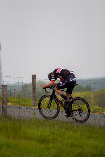 A person is riding a black and red bicycle through a field with the number 29 on their back.