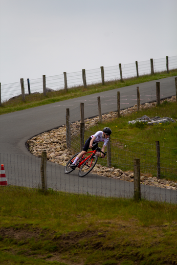 A cyclist wearing a black helmet is racing his red and black bicycle down a hill.