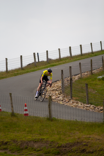 A man wearing a yellow and black shirt is riding a bicycle down a steep road.