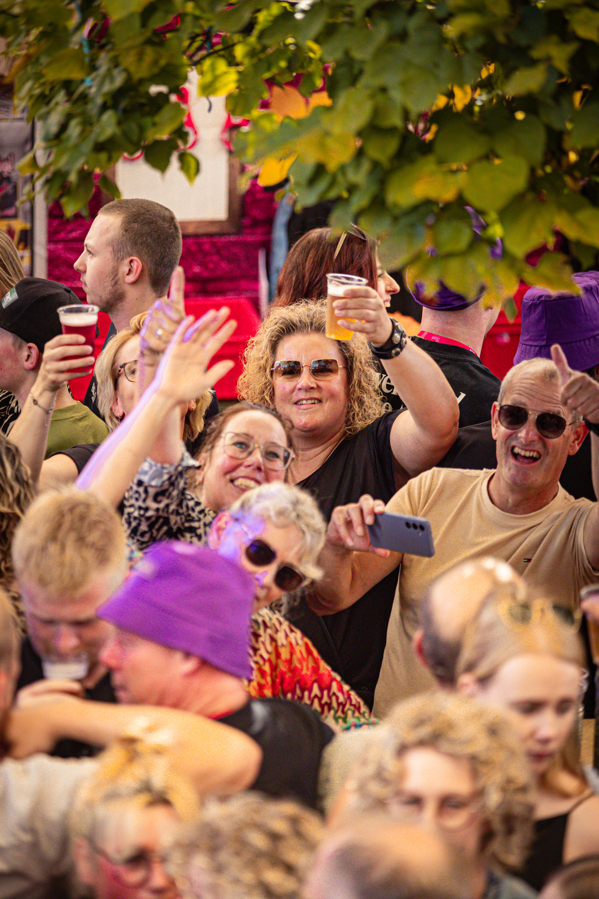 A lively scene at an outdoor event with people waving, smiling and taking selfies. The atmosphere is vibrant and energetic.