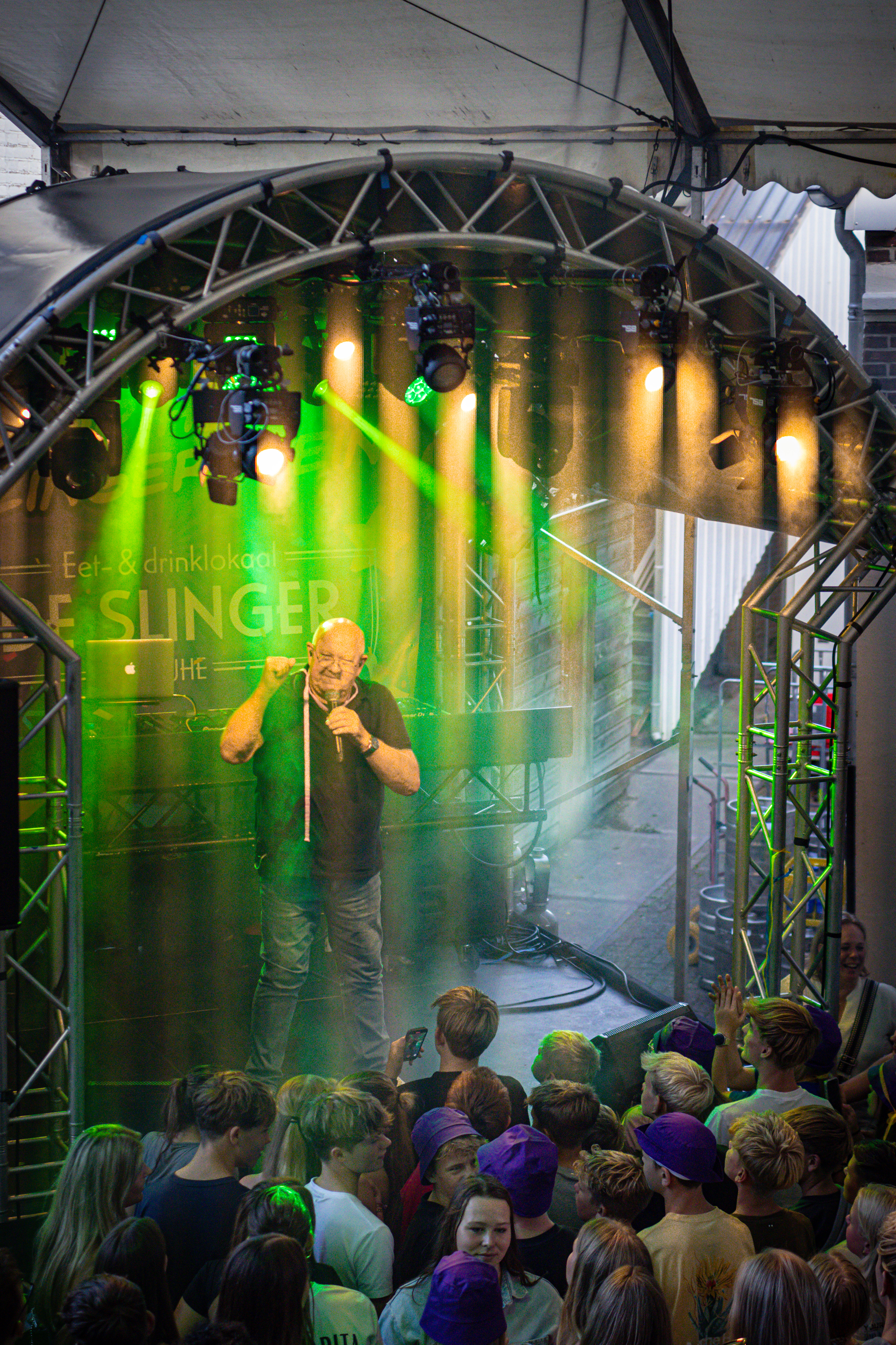 A man on stage with a microphone in front of a banner reading Slinger.