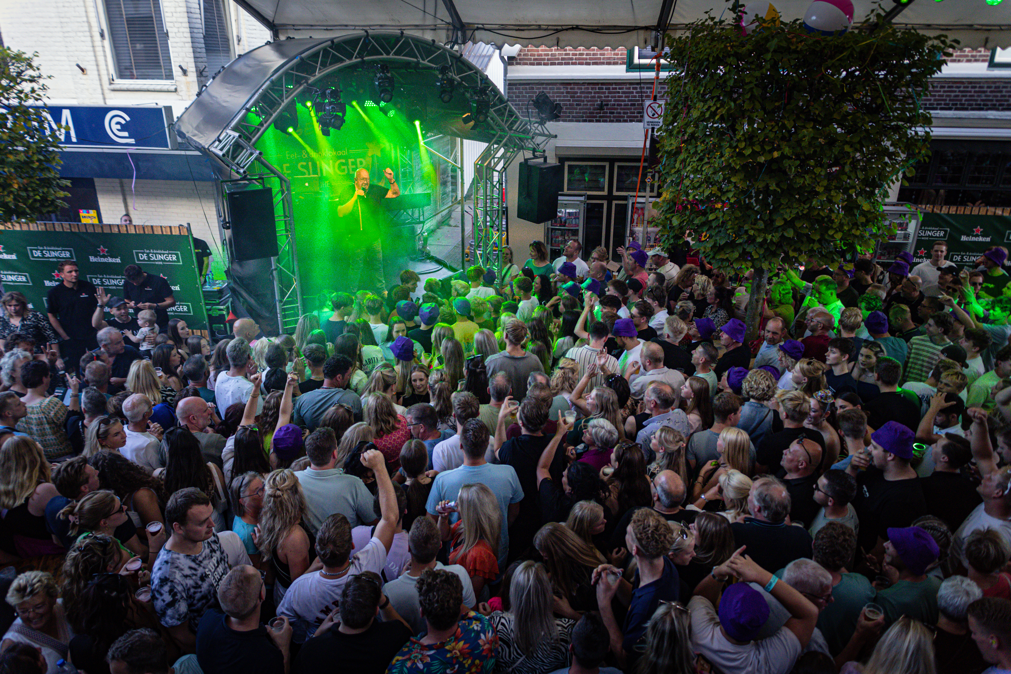 A large crowd at a concert, the stage is bathed in green lights and there are people playing instruments.