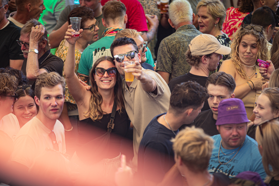 A group of people celebrating a wedding, some are holding drinks and others have sunglasses on.