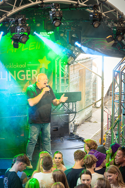 A man is singing on a stage with a banner that says drinkkaal.